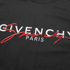 Close-up of a black tee adorned with the Givenchy Paris Signature embroidered logo. The word "Givenchy" stands in large white lettering, "Paris" appears below in smaller print, and it is accented by a stylish red script. This piece, crafted from premium cotton, showcases printed branding at its finest.