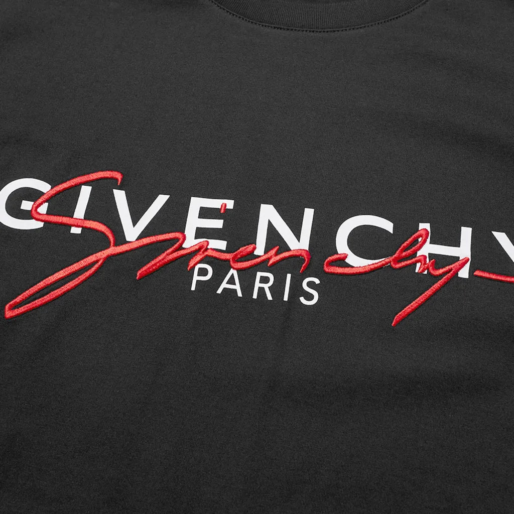Close-up of a black tee adorned with the Givenchy Paris Signature embroidered logo. The word "Givenchy" stands in large white lettering, "Paris" appears below in smaller print, and it is accented by a stylish red script. This piece, crafted from premium cotton, showcases printed branding at its finest.