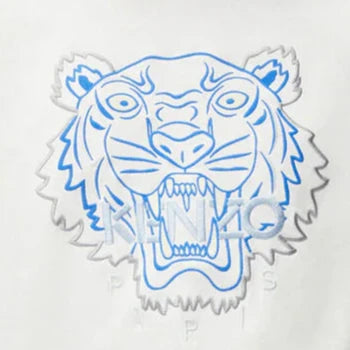 The Kenzo Embroidered Tiger T-Shirt in white showcases a detailed illustration of a tiger's head, mouth open, skillfully embroidered in blue lines. The design is highlighted by the word "KENZO," offering a premium cotton feel typical of this Kenzo brand staple.