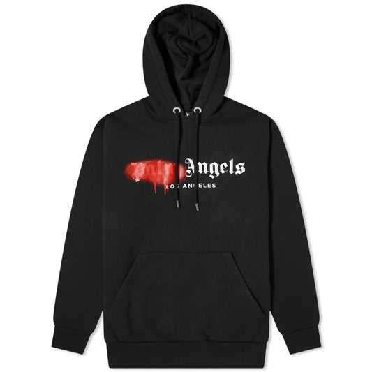 The Palm Angels Tokyo Sprayed Logo Hoodie is crafted from premium heavyweight black cotton, featuring the text "Angels Los Angeles" in a stylized white font with a distinctive red, paint-like smear obscuring where "Palm" would appear. This hoodie includes a front pocket and drawstrings on the hood.