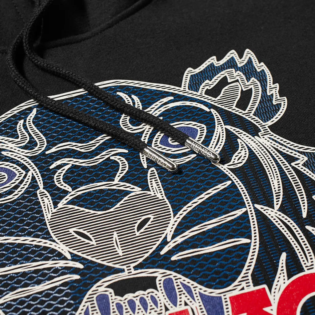 Close-up of the Kenzo Silicone Scuba Hoodie, showcasing a black fabric with an embroidered blue and white tiger face design characterized by intricate line art details, evoking the iconic style of Kenzo. Two black drawstrings with metallic tips partially obscure the tiger motif, while the textured background enhances depth.