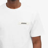 A person in a white Jacquemus Gros Grain Logo T-Shirt made from organic cotton, showcasing the embroidered logo on the upper left. The background is plain white.