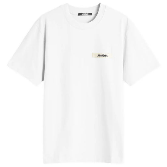 Jacquemus Gros Grain Logo T-Shirt White by Jacquemus features a white, organic cotton design with short sleeves and a small beige rectangular patch on the front showcasing an embroidered grosgrain logo in black lettering.
