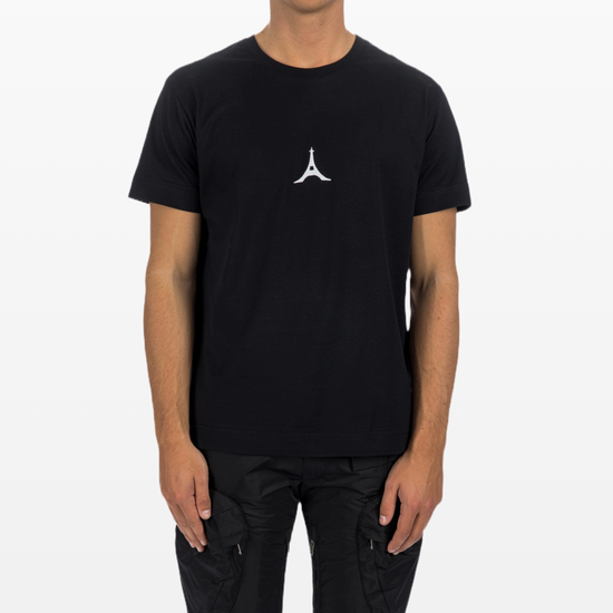 A person is casually styled in a black Givenchy Paris Eiffel College Logo T-Shirt, featuring a subtle white Eiffel Tower graphic on the front. They pair it with black trousers, effortlessly elevating their casual wardrobe against a plain white background.