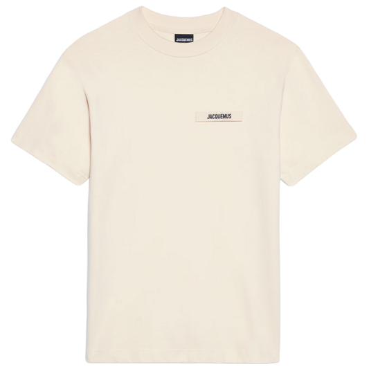 The Jacquemus Gros Grain Logo T-Shirt in beige, crafted from organic cotton, has short sleeves, a round neckline, and features a small rectangular label on the front with the "Jacquemus" brand name.