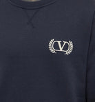 Close-up of the Valentino Varsity V Logo Sweatshirt in dark blue by Valentino, featuring elegant embroidered branding with a white "V" accompanied by two laurel branches on the chest.