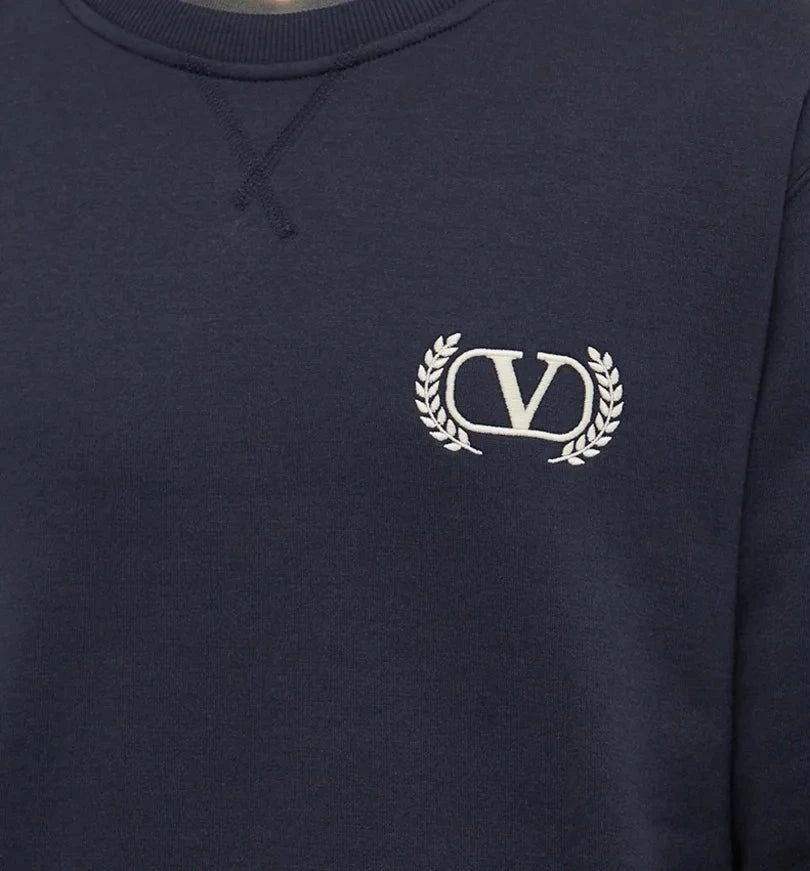 Close-up of the Valentino Varsity V Logo Sweatshirt in dark blue by Valentino, featuring elegant embroidered branding with a white "V" accompanied by two laurel branches on the chest.