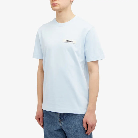 A person in a black Jacquemus Gros Grain T-Shirt featuring a small logo on the chest and jeans, positioned against a plain white background.