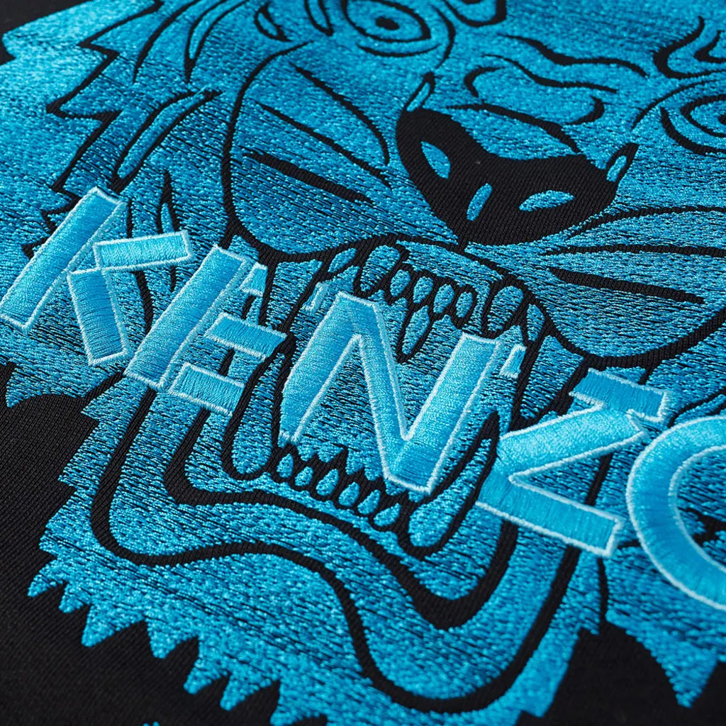 A close-up of a vibrant blue embroidered tiger face on a black Kenzo Neon Tiger Embroidered Sweatshirt, featuring the bold, textured letters "KENZO" overlaying the design. The tiger's fierce expression showcases intricate detailing and contrasting colors, epitomizing Kenzo's Embroidered Branding at its finest.