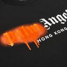 A detailed view of the Palm Angels Hong Kong Sprayed Logo T-Shirt captures the essence of streetwear fashion. The word "Palm" is highlighted by an orange graffiti-style effect accented with paint drips, while "Angels Hong Kong" is elegantly presented in crisp white Gothic lettering. Perfect for those who crave edgy style, this tee is a must-have for fashion enthusiasts.