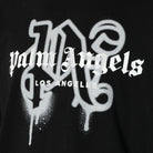The Palm Angels Los Angeles Monogram Sprayed Logo T-Shirt is a black cotton jersey piece that showcases the iconic "Palm Angels Los Angeles" in a white Gothic-style font. The lettering features a spray-paint effect with subtle drips, emphasizing an edgy Los Angeles monogram vibe.