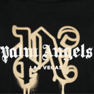 The Palm Angels Las Vegas Monogram Sprayed Logo T-Shirt showcases a black background adorned with the iconic Palm Angels logo in white ornate Gothic font. Below the logo, "Las Vegas" is displayed in smaller white block letters, complemented by gold stylized lettering elements that create a luxurious Las Vegas Monogram effect against the dark backdrop.