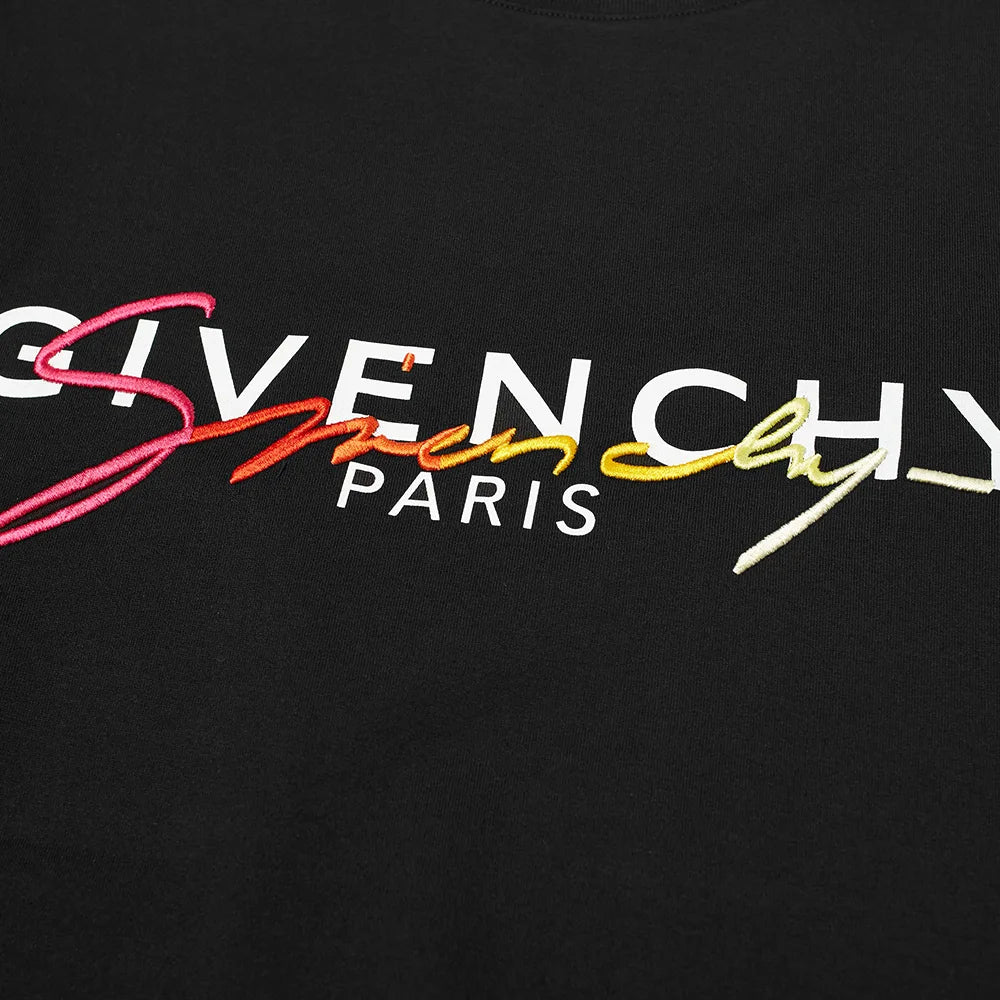 A close-up of the Givenchy Paris Signature Embroidered Logo T-Shirt highlights the premium black cotton fabric, featuring the word "GIVENCHY" in white with "PARIS" beneath it. The shirt is beautifully embellished with a colorful embroidered script overlaying the letters, enhancing this exquisite design with a touch of printed branding.