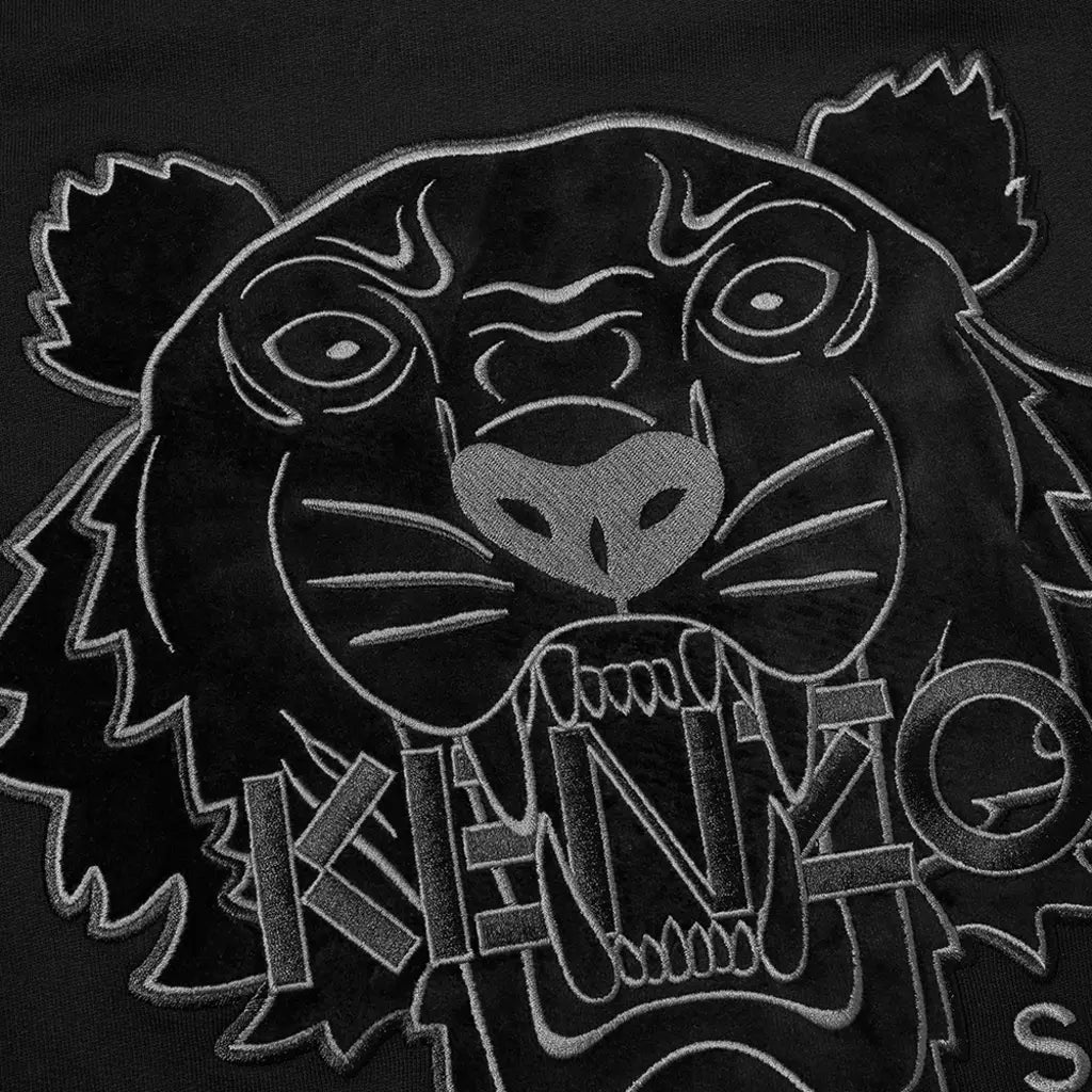 The Kenzo Velvet Tiger Sweatshirt by Kenzo features an embossed black fabric adorned with a stylized velvet tiger's face, its mouth ajar. "KENZO" is seamlessly integrated into the design beneath it. Crafted from pure cotton, the detailed monochromatic embroidery provides a bold and striking look.