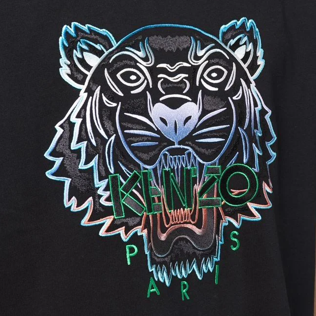 The Kenzo Gradient Embroidered Tiger T-Shirt showcases a stylized tiger face with an open mouth, intricately embroidered on a black fabric. The words "KENZO" are boldly stitched in green letters below the tiger, followed by "PARIS." This piece features striking blue and white outlines, embodying high-quality craftsmanship and was made in Portugal.