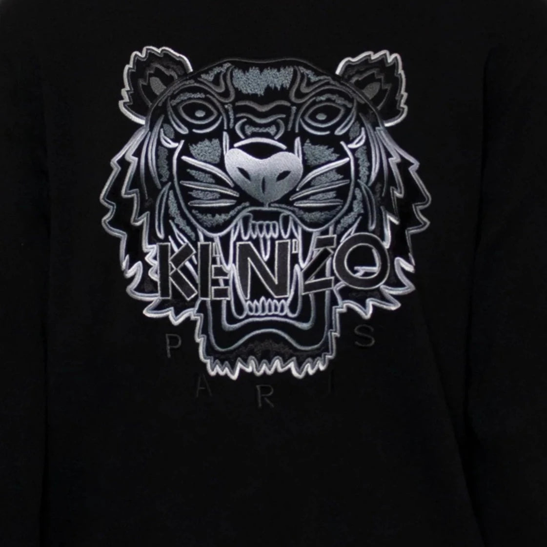 The Kenzo Gradient Tiger Embroidered Sweatshirt showcases Parisian flair with its detailed silver and gray tiger head embroidery. The bold "KENZO" branding is prominently featured across the face, accompanied by the partially visible "PARIS" beneath.