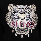 The Kenzo Varsity Tiger Sweatshirt features embroidered branding with a striking tiger head in black and white against a black background. The words "KENZO PARIS" are displayed in red and white, capturing the essence of Parisian style.