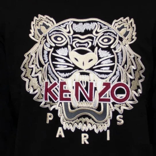 The Kenzo Varsity Tiger Sweatshirt features embroidered branding with a striking tiger head in black and white against a black background. The words "KENZO PARIS" are displayed in red and white, capturing the essence of Parisian style.