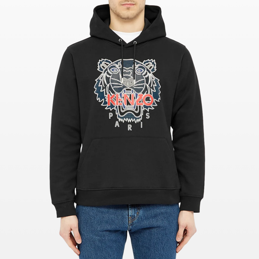 A person is wearing a Kenzo Silicone Scuba Hoodie, which showcases a stylized tiger design adorned with the "KENZO PARIS" text, paired with blue jeans. The black hoodie features a silicone detailed print, front pocket, and drawstrings.