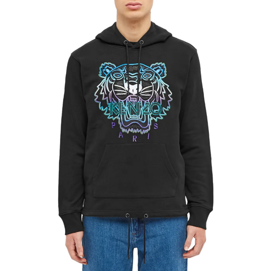 Dressed in the Kenzo Holiday Capsule Limited Edition Tiger Embroidered Hoodie, a person displays a beautifully stitched tiger face in shades of blue and purple, with "Kenzo Paris" elegantly scripted beneath it. Paired with blue jeans, they pose against a simple white backdrop.