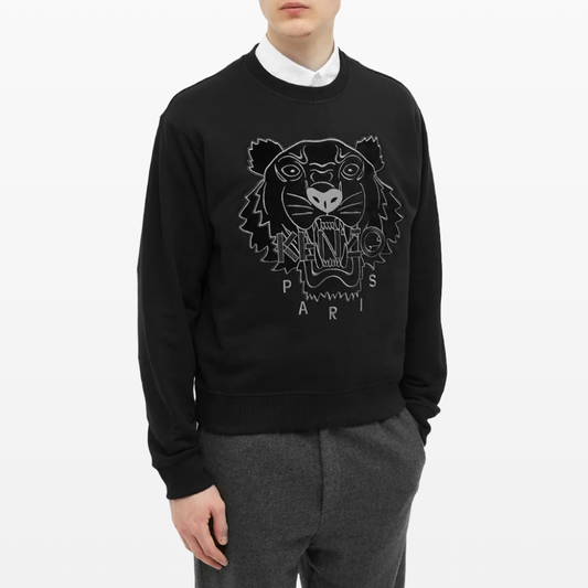 A person is dressed in a Kenzo Velvet Tiger Sweatshirt, which displays a velvet tiger face design along with the word "Paris," and it is paired with gray trousers.