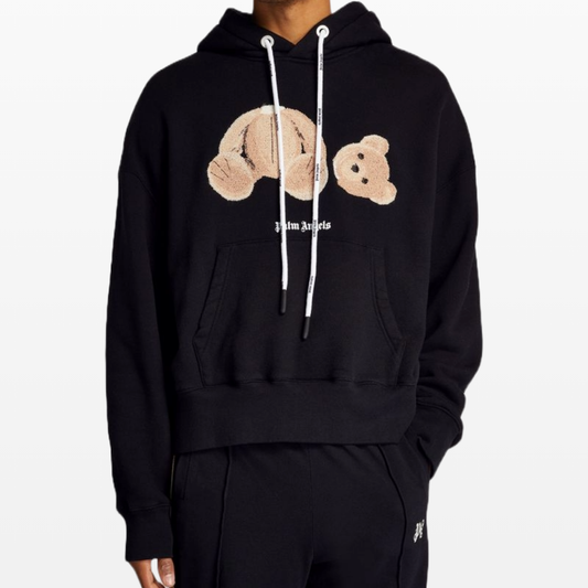 A person wearing a Palm Angels Bear Hoodie exudes confidence with its playful teddy bear design, featuring the iconic detached head and body embroidered on the chest. Hands in pockets, they showcase a chic fusion of streetwear and high fashion by Palm Angels.