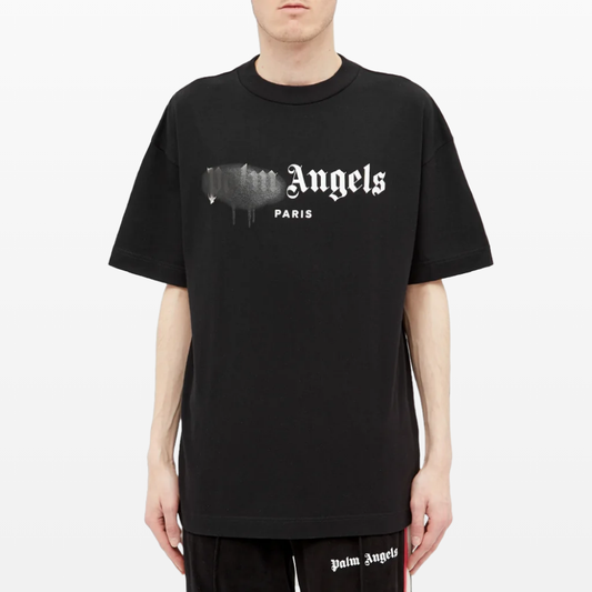 A person is rocking the streetwear style in a Palm Angels Paris Sprayed Logo T-Shirt, featuring "Palm Angels" and "PARIS" with a paint drip effect. Their ensemble is completed with black shorts emblazoned with "Palm Angels.