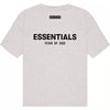 The Fear of God ESSENTIALS SS22 T-Shirt in Light Oatmeal showcases "ESSENTIALS" in bold black letters with "FEAR OF GOD" subtly printed below, both positioned on the back. Designed under Jerry Lorenzo's creative direction, this iconic piece captures the essence of the Fear of God Essentials aesthetic.