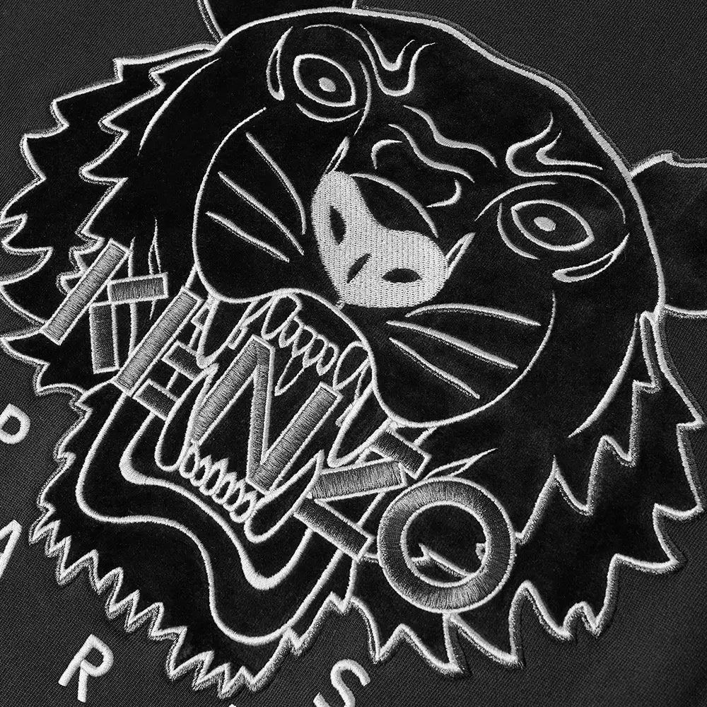 A close-up view reveals the fierce roar of a black and white embroidered tiger on the Kenzo Festive Tiger Sweatshirt. Crafted from premium cotton, this piece showcases detailed stitching that accentuates the tiger's bold expression alongside the integrated "KENZO" lettering, epitomizing both luxury and artistry.