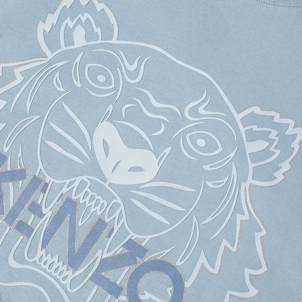Close-up of a pale blue luxe cotton fabric showcases the iconic Kenzo tiger logo, with a stylish white outline of the roaring tiger's face. The lower portion reveals partially visible text saying "KENZO," capturing the bold essence of the Kenzo Classic Festive Tiger T-Shirt.