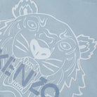Close-up of a pale blue luxe cotton fabric showcases the iconic Kenzo tiger logo, with a stylish white outline of the roaring tiger's face. The lower portion reveals partially visible text saying "KENZO," capturing the bold essence of the Kenzo Classic Festive Tiger T-Shirt.