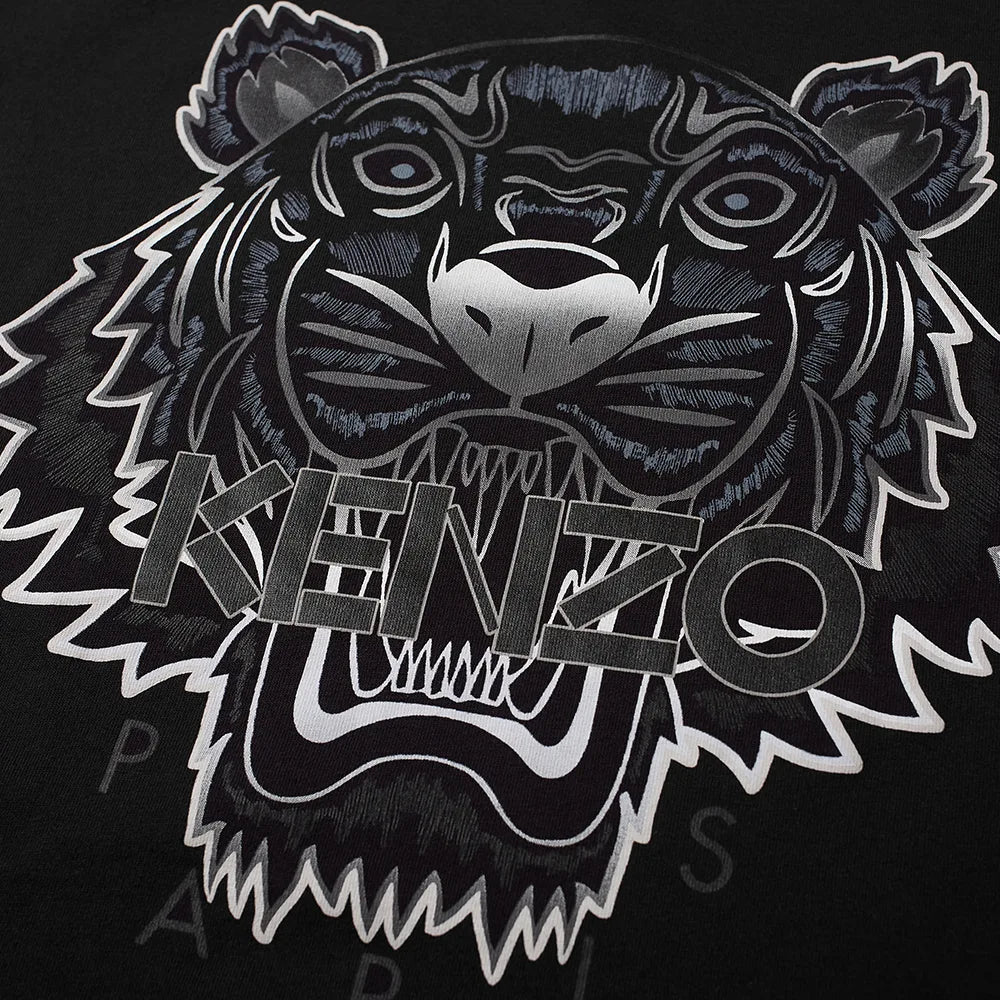 Close-up of the Kenzo Gradient Tiger T-Shirt in black, showcasing a fierce tiger's face with "KENZO" prominently displayed. This Parisian brand enhances the design by adding depth with silver-highlighted eyes and teeth, creating a striking contrast against the dark background.