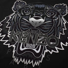 Close-up of the Kenzo Gradient Tiger T-Shirt in black, showcasing a fierce tiger's face with "KENZO" prominently displayed. This Parisian brand enhances the design by adding depth with silver-highlighted eyes and teeth, creating a striking contrast against the dark background.