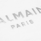 A detailed close-up of the Balmain Logo Print Round Neck T-Shirt, Silver, highlights the luxurious cotton fabric with "Balmain Paris" elegantly displayed in a striking silver foil print.