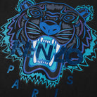 The Kenzo Holiday Capsule Tiger T-Shirt showcases an electric blue tiger face with sharp teeth in shades of blue and black, overlaid with the text "KENZO PARIS." The vibrant illustration stands out against the sleek black background of this streetwear piece from Kenzo.
